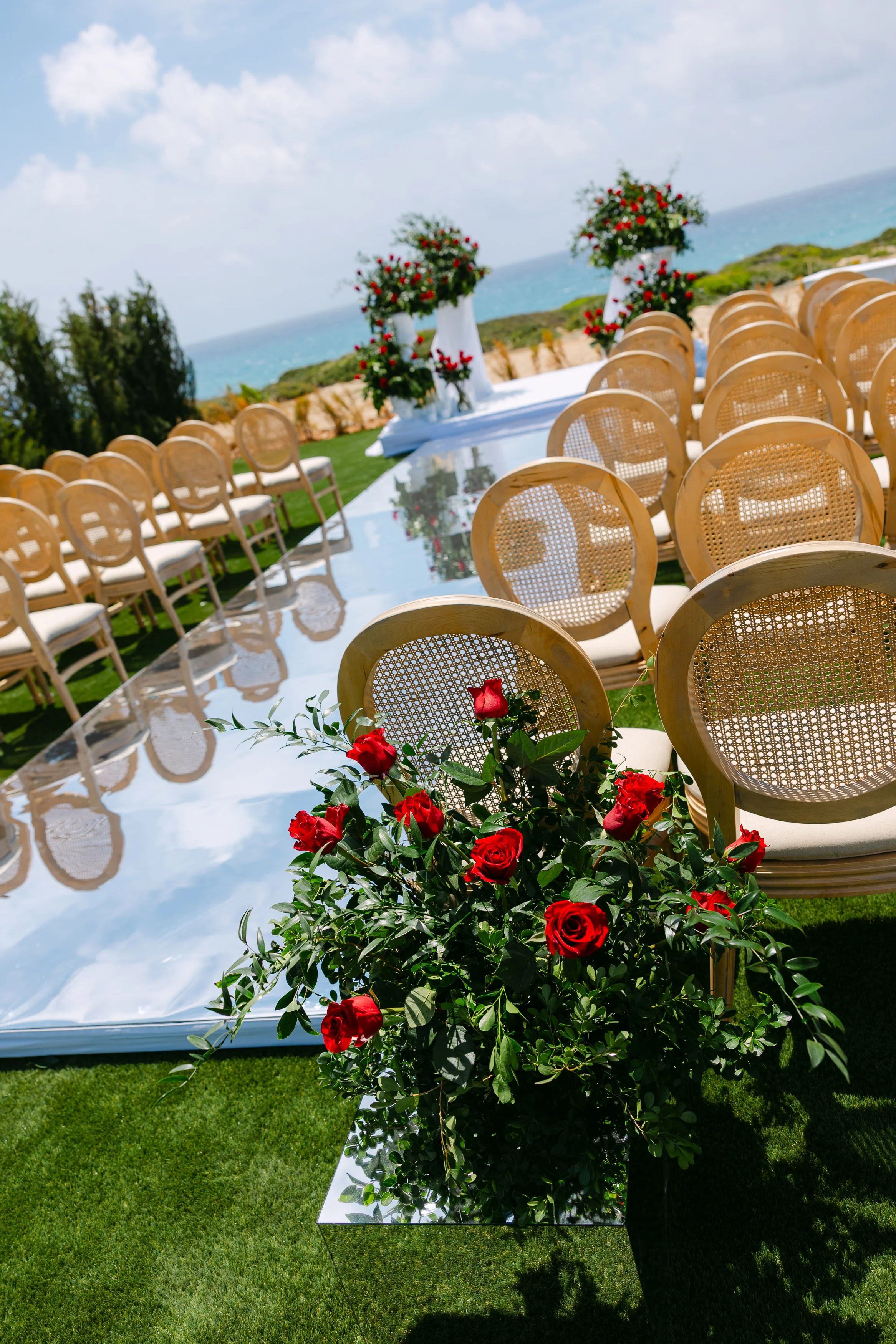 Aisle perspective at Ozea with red rose pedestals against cane-back chairs.