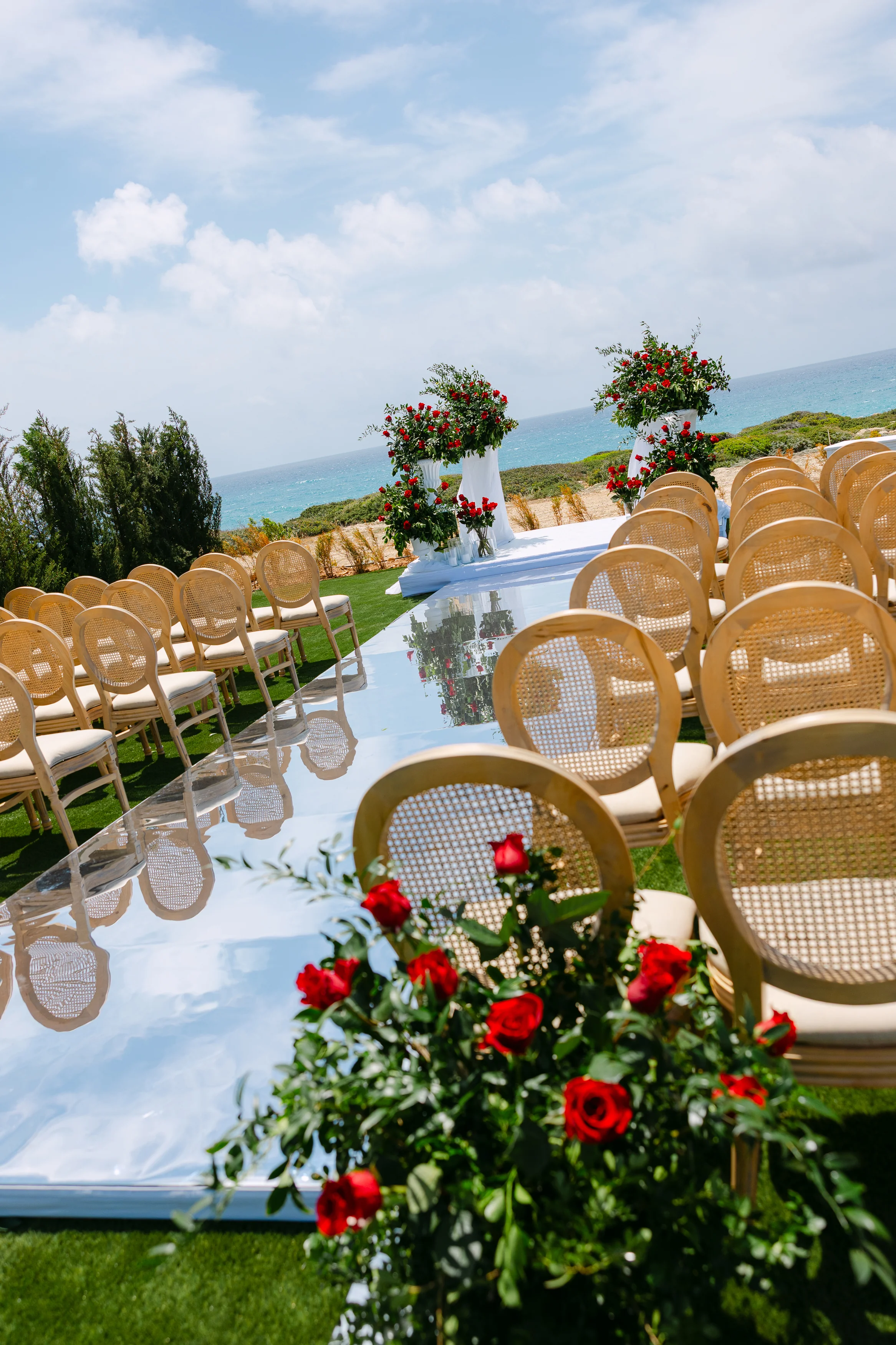 Angled view down the ceremony aisle at Ozea with rose pedestals and cane chairs.