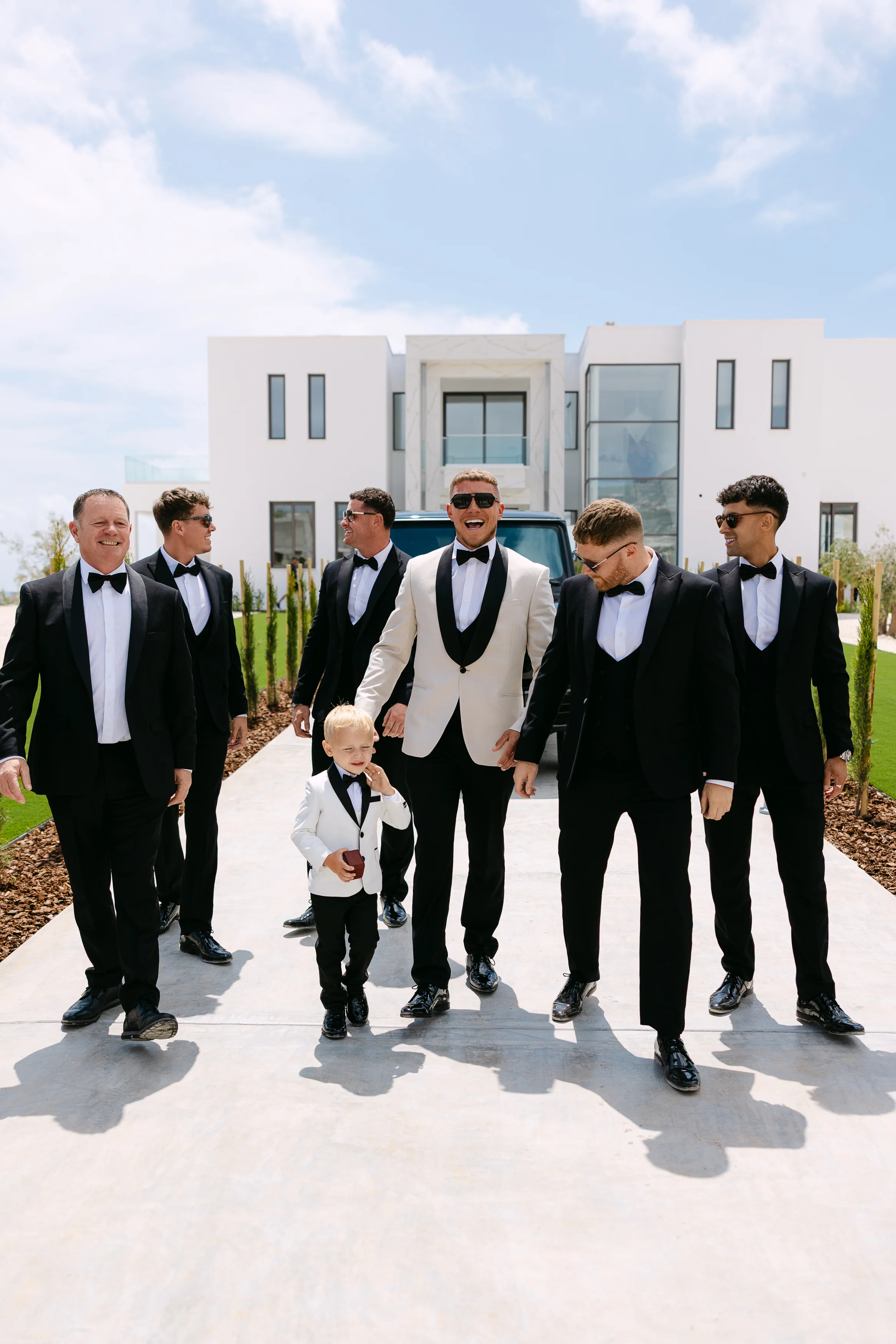 Groom and groomsmen walking together on the venue driveway at OZEA with the young ring bearer.