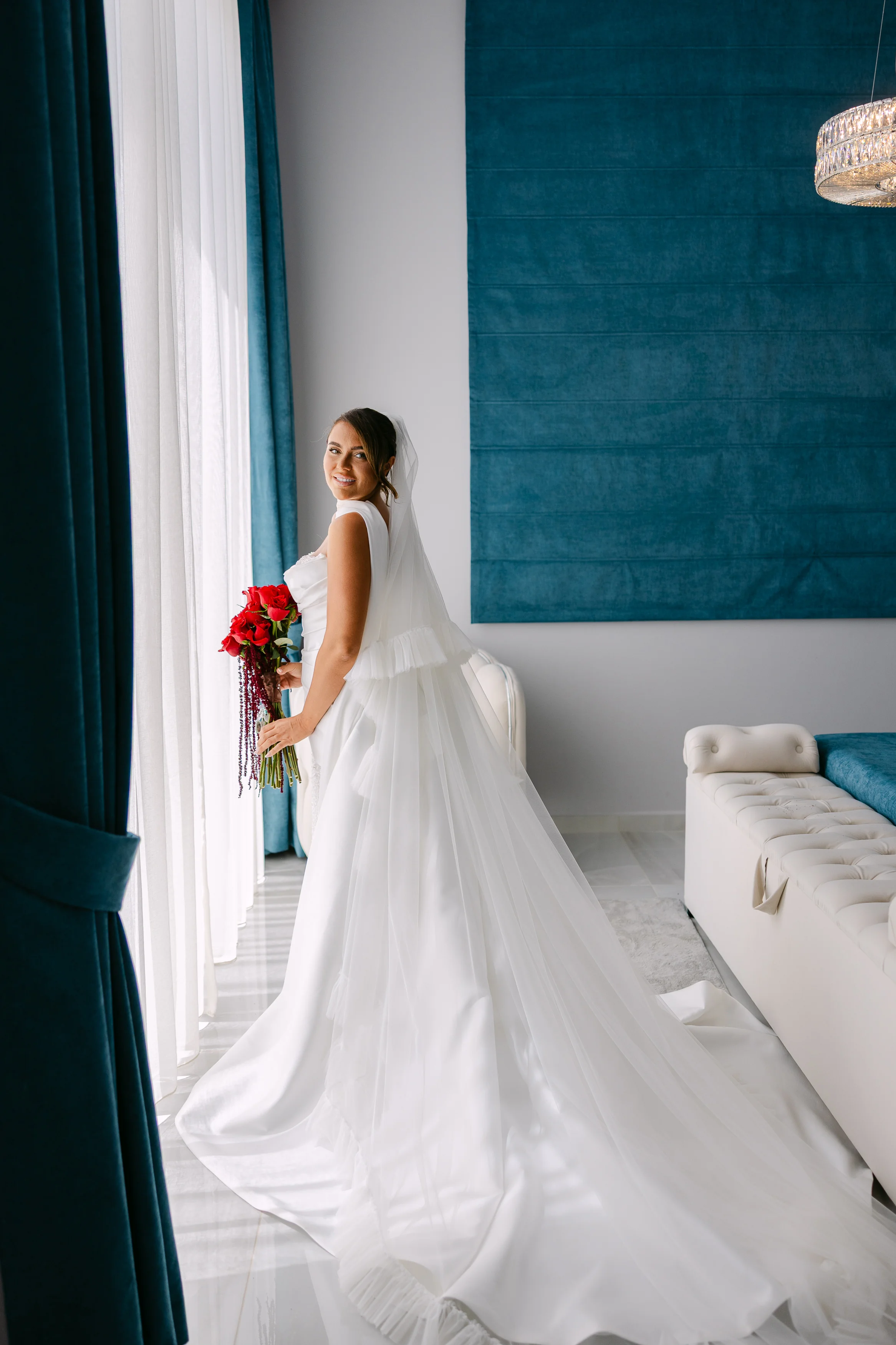Bride in her gown holding a red bouquet inside the bridal suite at OZEA.