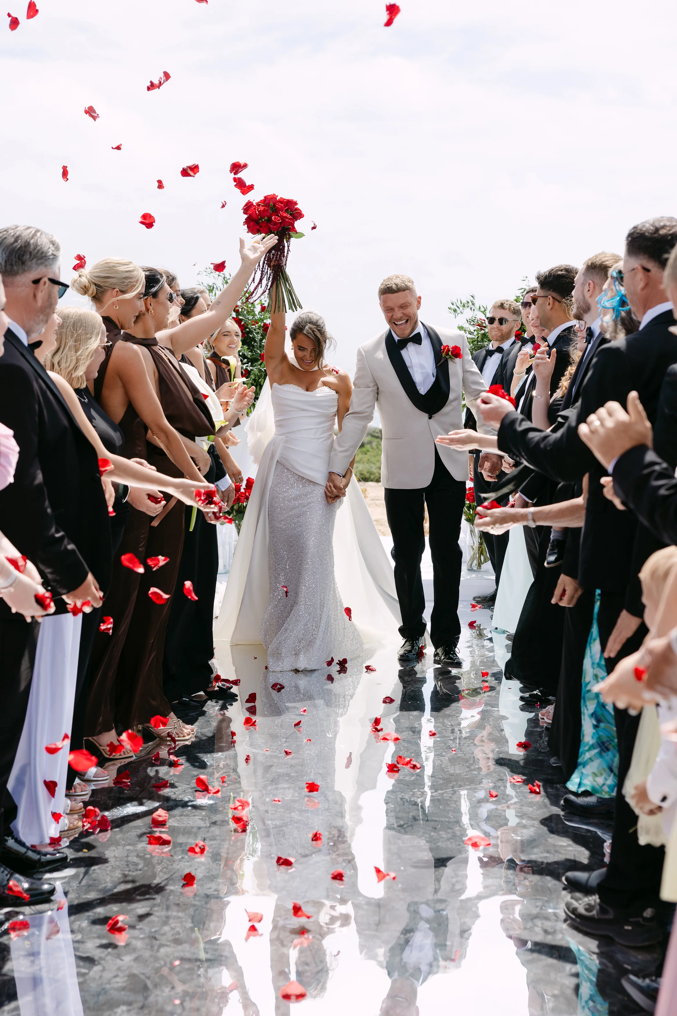 Bride lifting her red rose bouquet during the confetti exit at Ozea.