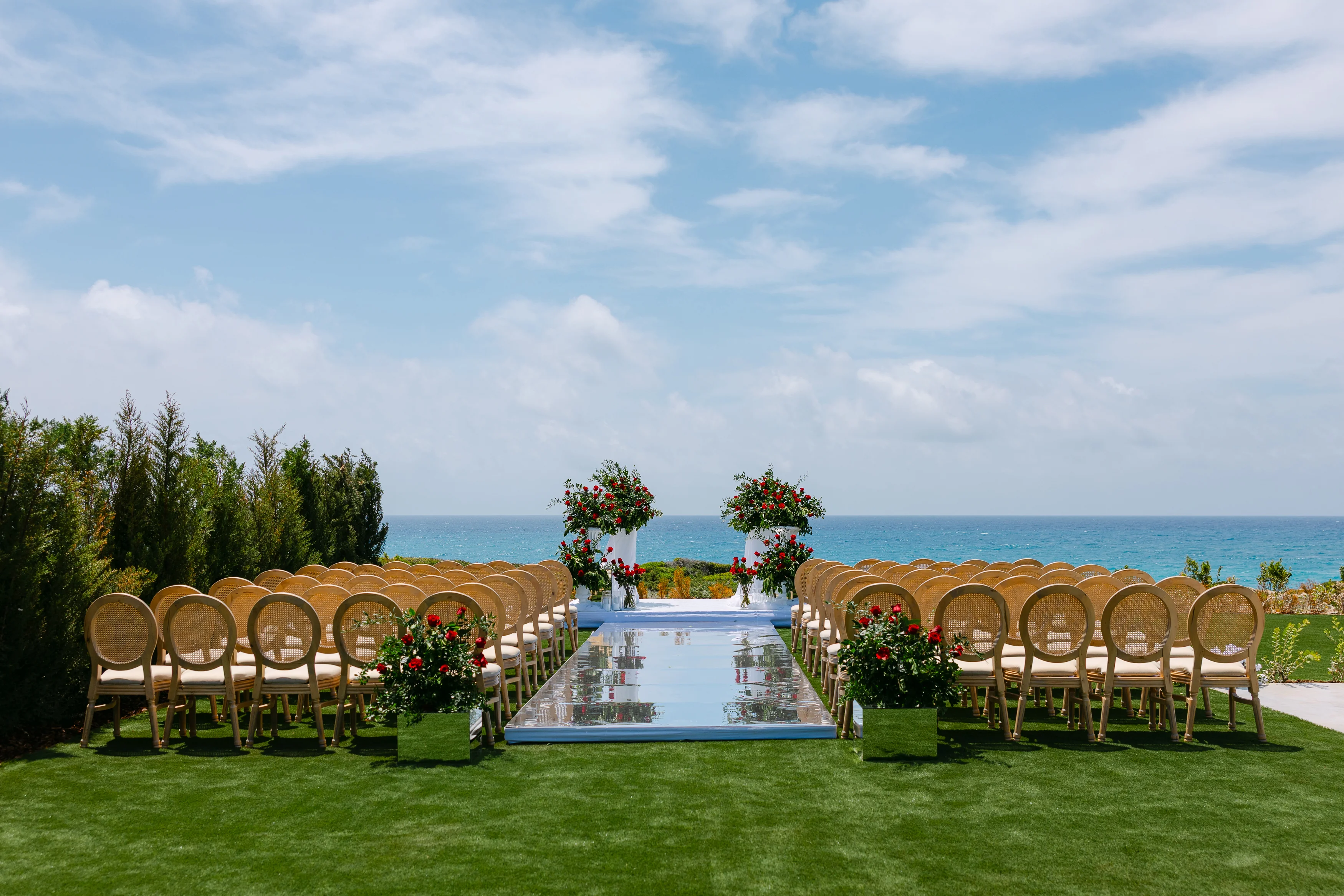 Wide view of the wedding ceremony aisle at OZEA with chairs facing the sea and floral arrangements at the altar.