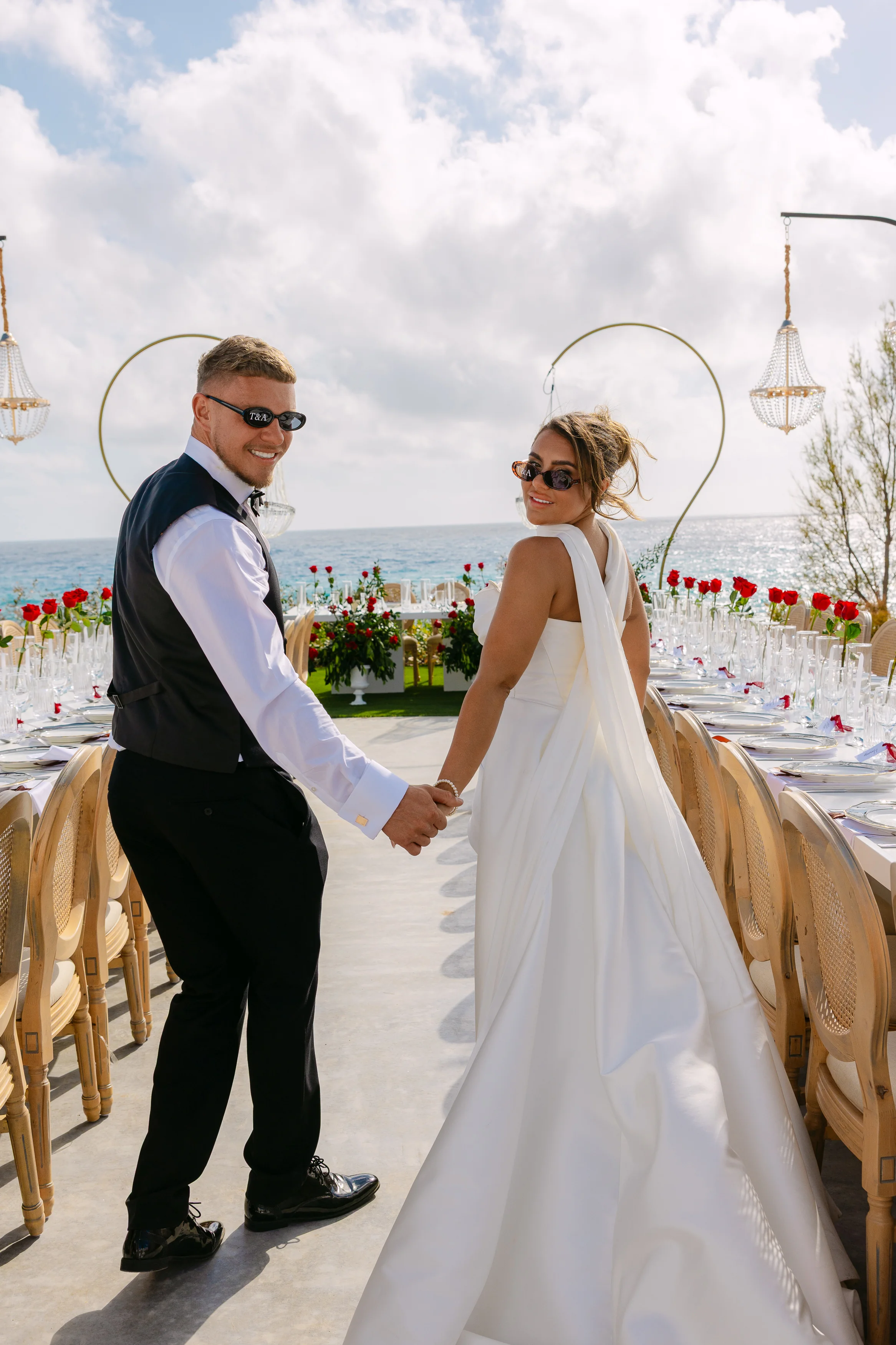 Bride and groom turning back at the head of the banquet table at Ozea with the sea behind.
