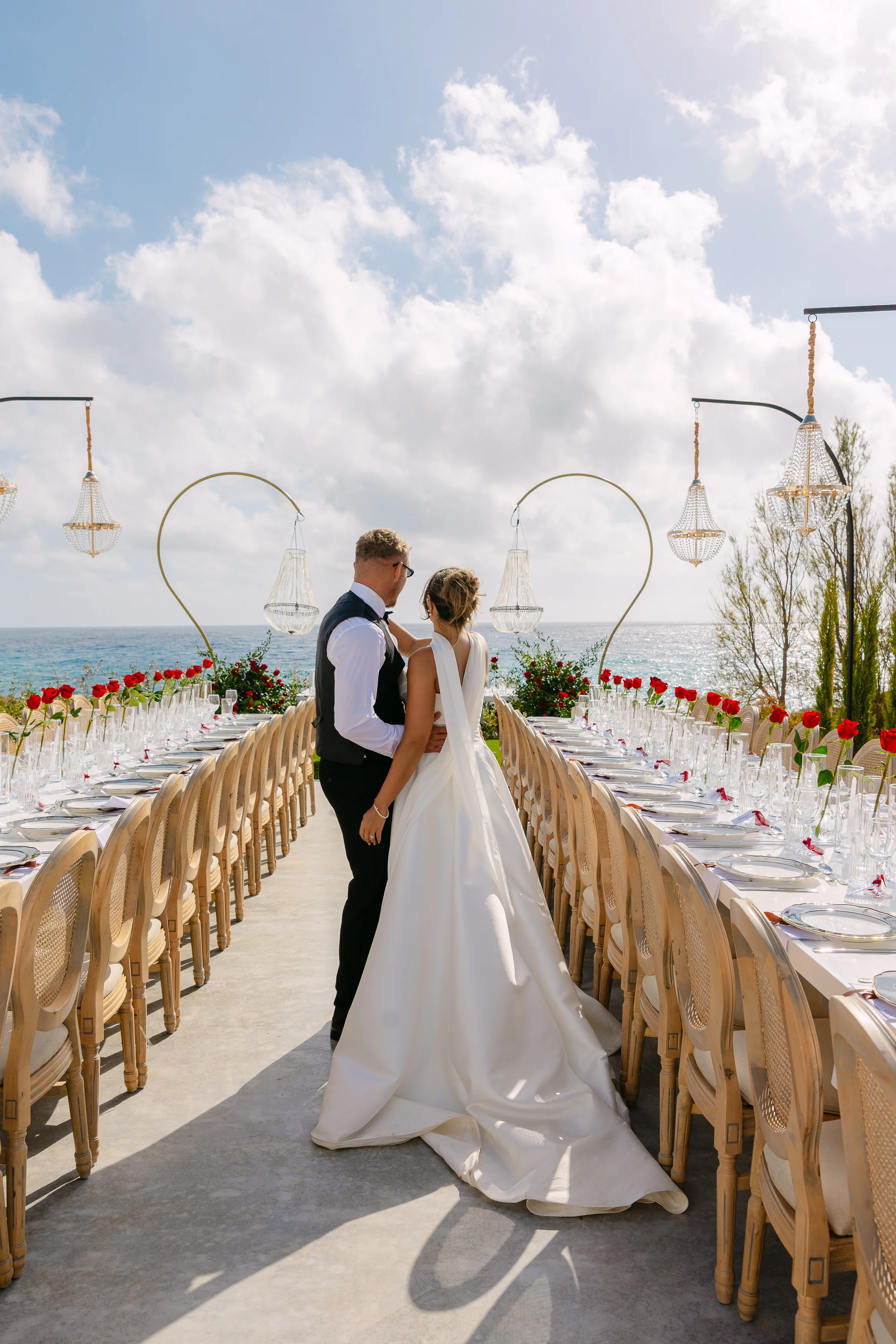 Bride and groom standing together at the end of the banquet table at OZEA, looking out toward the Mediterranean.