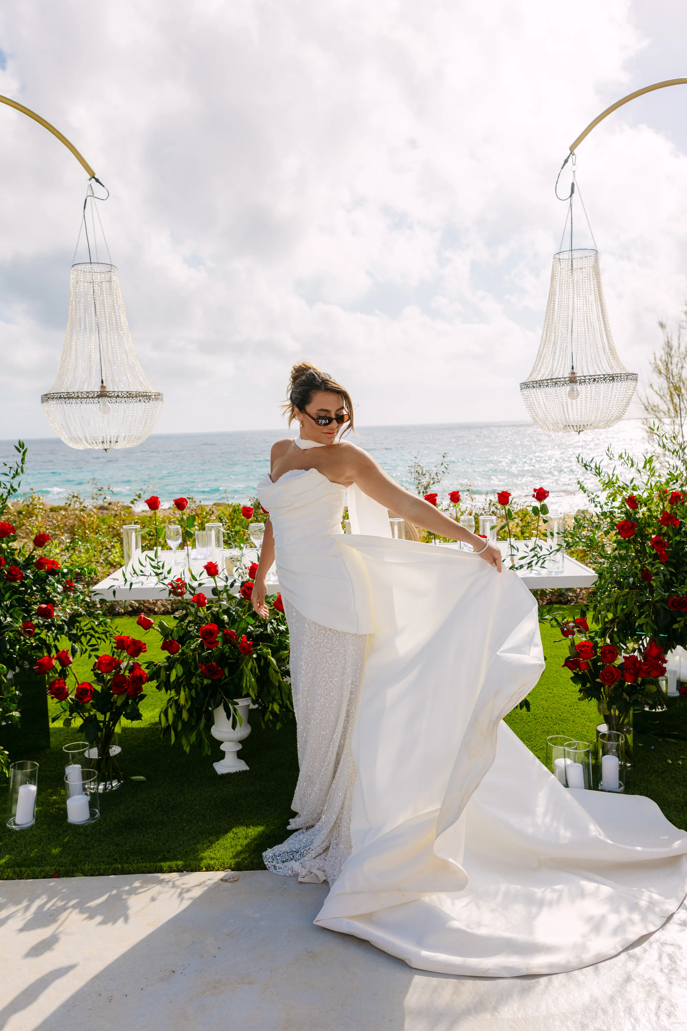 Bride twirling her dress at the head of the banquet at OZEA, framed by crystal chandeliers and red rose lined tables.