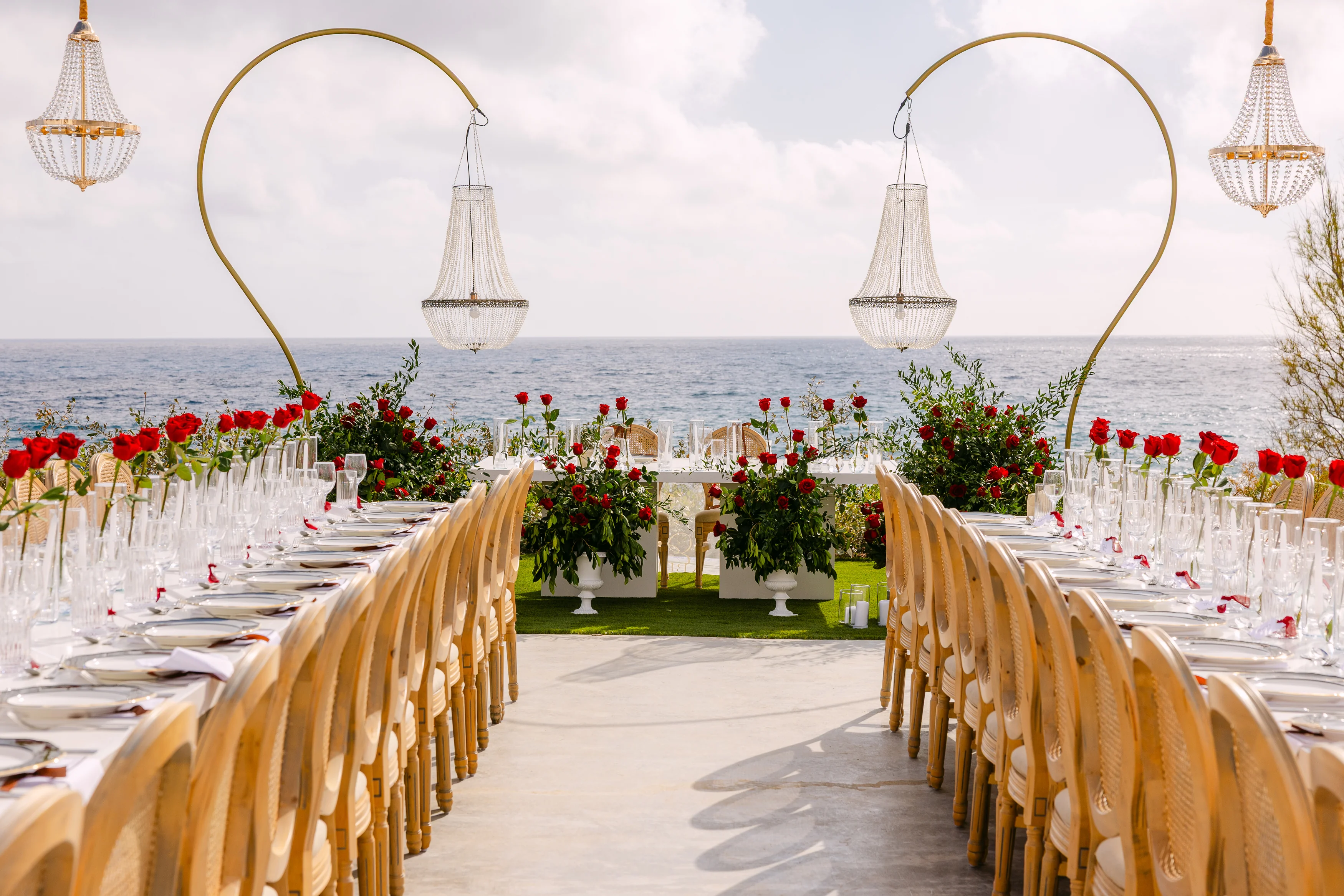 Long banquet tables at OZEA framed by tall arched chandeliers and the Mediterranean horizon.