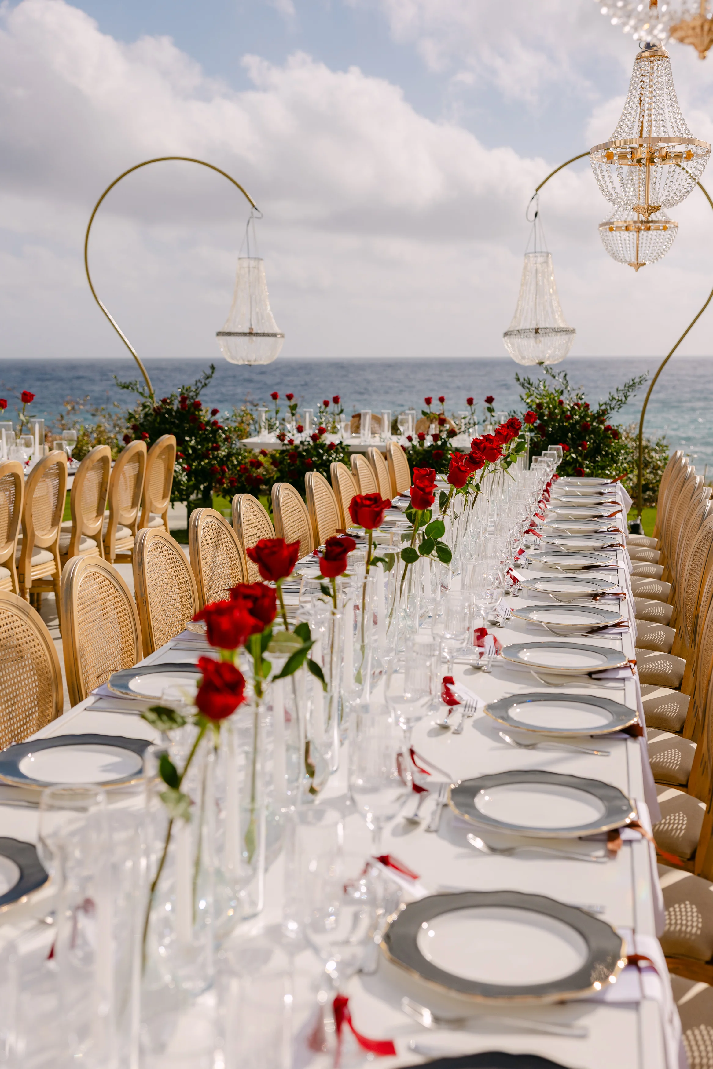 Vertical view of the long banquet table at OZEA with chandeliers, single roses, and the sea behind.