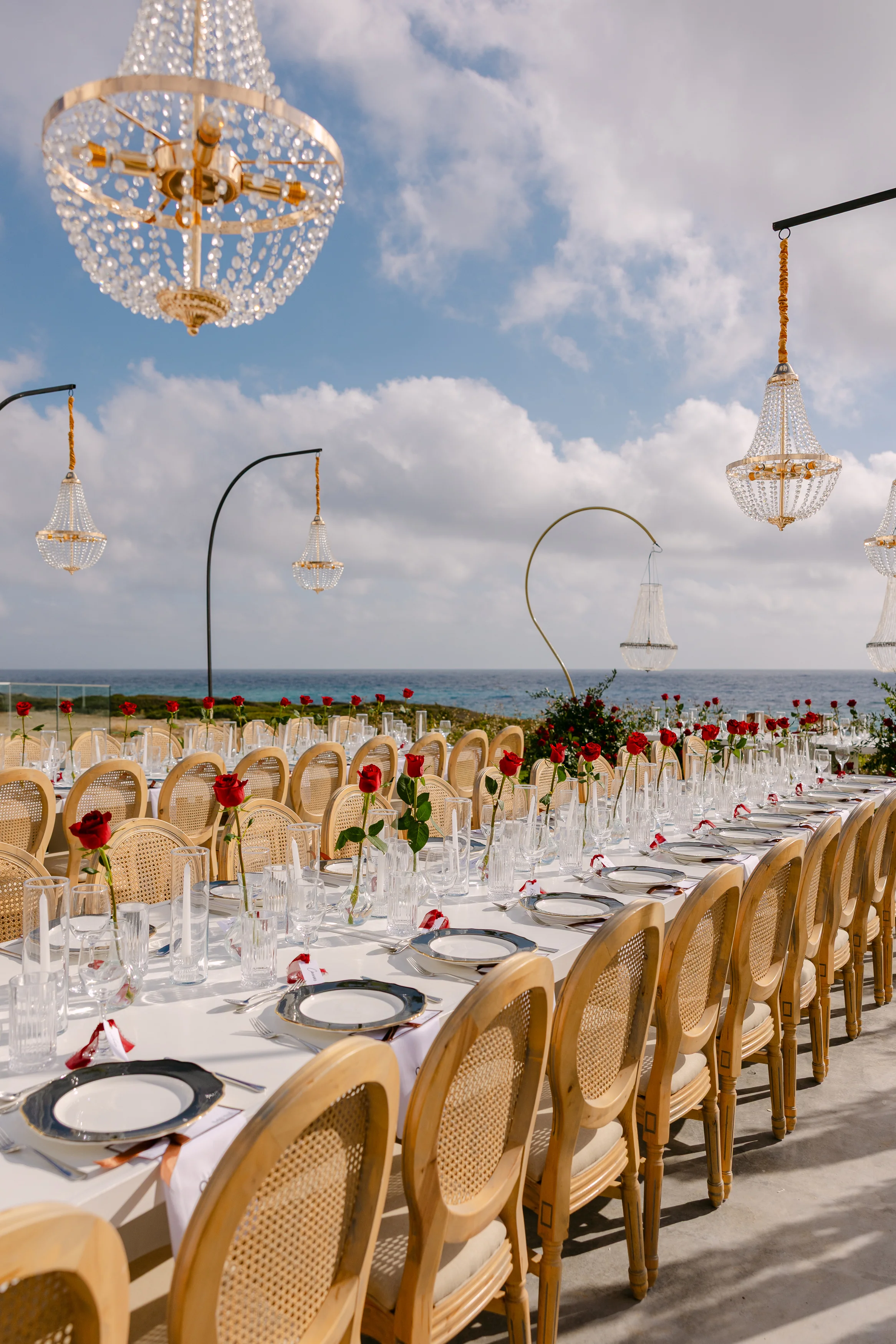 Close view of the crystal chandeliers above the banquet table at OZEA with the sea behind.