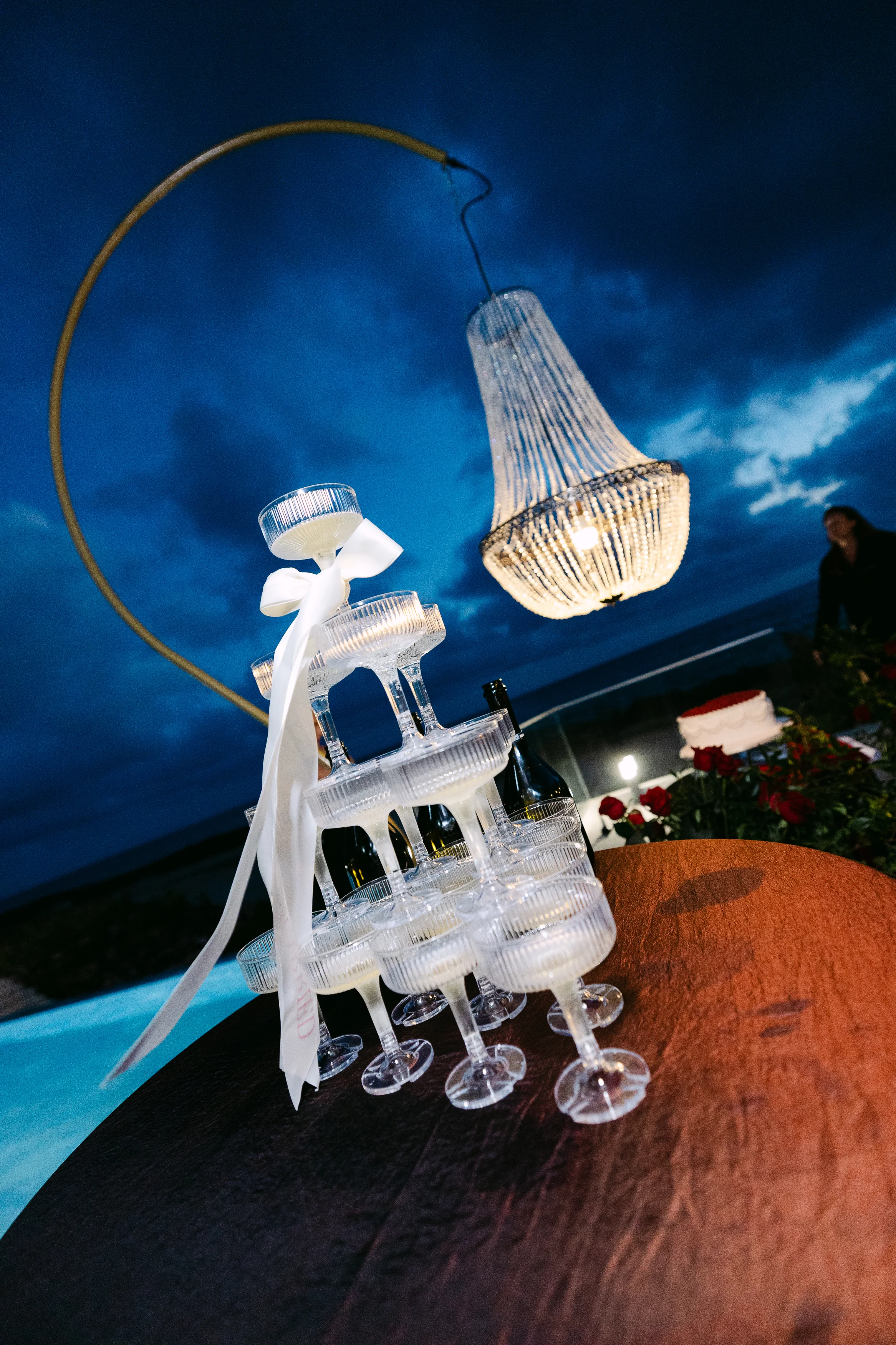 Champagne coupe tower at Ozea photographed at dusk beneath a chandelier with the sea behind.