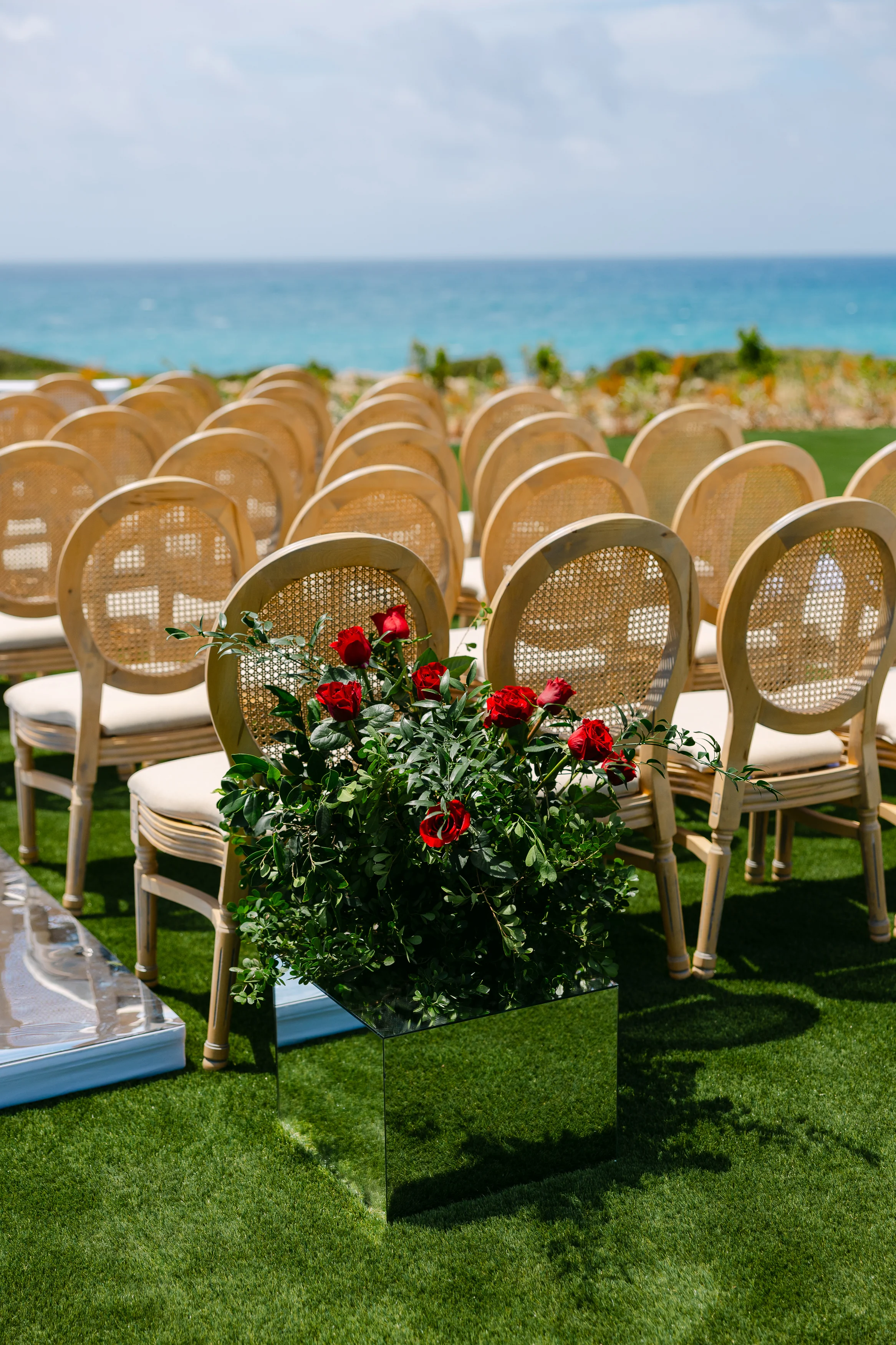 Ceremony chairs at Ozea with a red rose arrangement on a mirrored cube and the sea behind.